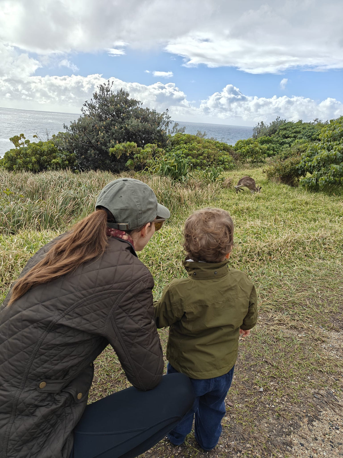 Woman and a young child on a grassy coastal headland looking out to sea