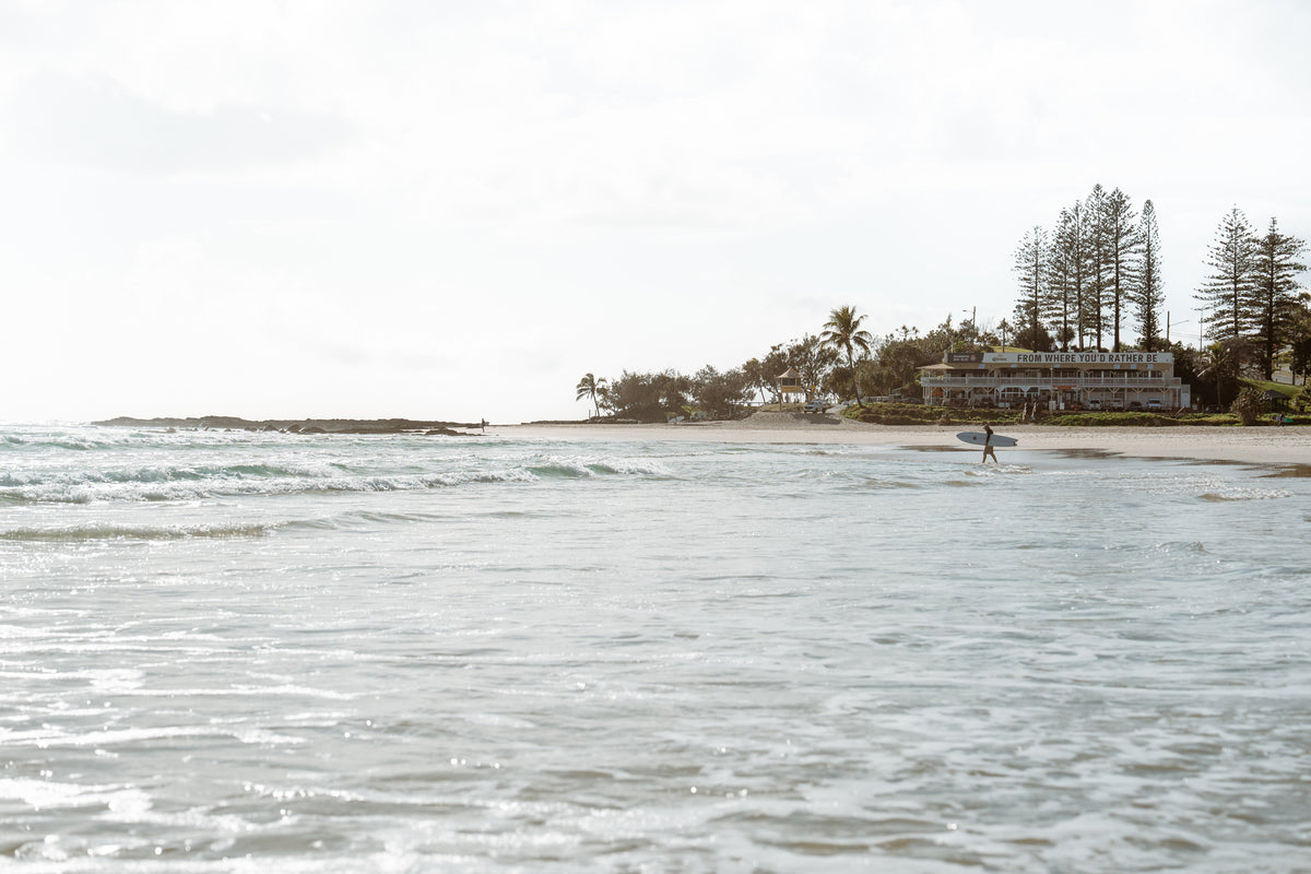 Surfer in the water off a palm-lined headland