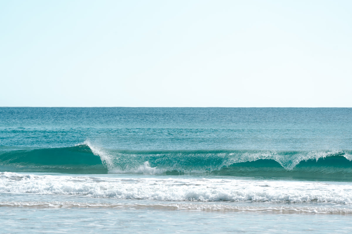 Waves breaking offshore under a clear blue sky