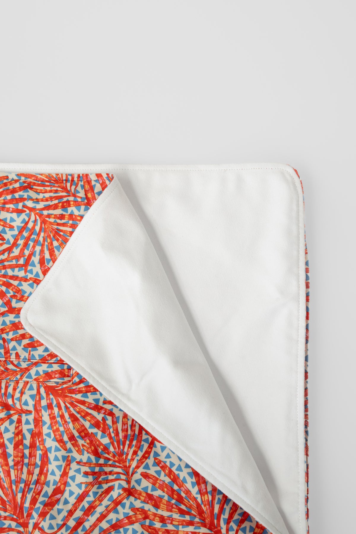 The Neren Towel in Coral Palms folded flat, showing the coral-red palm print and white reverse