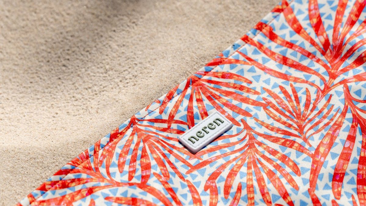 Close-up of the Neren Towel in Coral Palms on the sand, showing the coral-red palm print