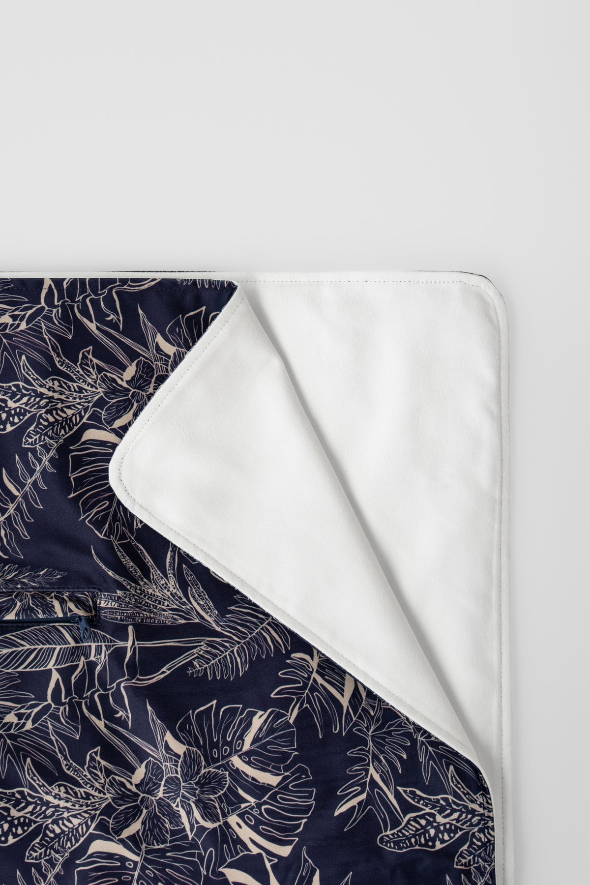 The Neren Towel in Midnight Tropics folded flat, showing the navy leaf print and white reverse